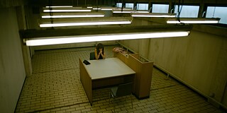 Still frame from the ZDF Series "Perfume" -"Perfume - Bondage": View from above into the interrogation room of the police. Elena Seliger (Natalia Belitski) sits at a table.