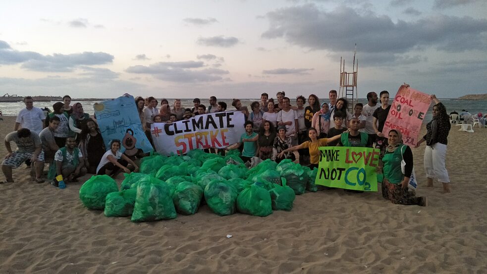 Un groupe de personnes sur la plage, brandissant des affiches pour la protection de l'environnement, devant eux des sacs remplis d'ordures.