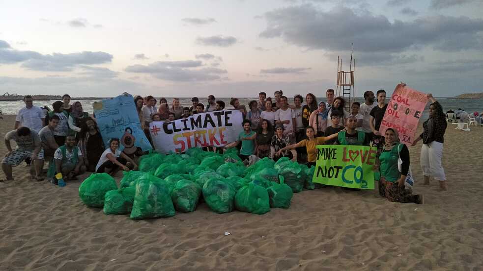 Eine Gruppe Umweltaktivist*innen am Strand mit Plakaten, vor ihnen Säcke voller Müll