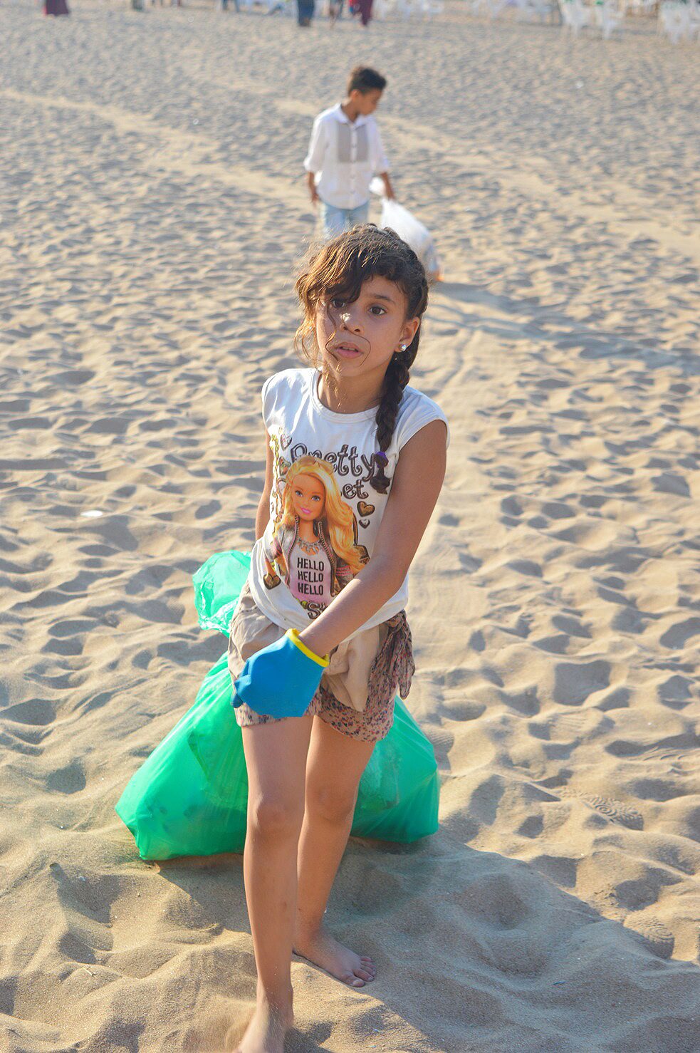 Une jeune fille portant des gants et portant un sac en plastique rempli d'ordures marchant vers la caméra.
