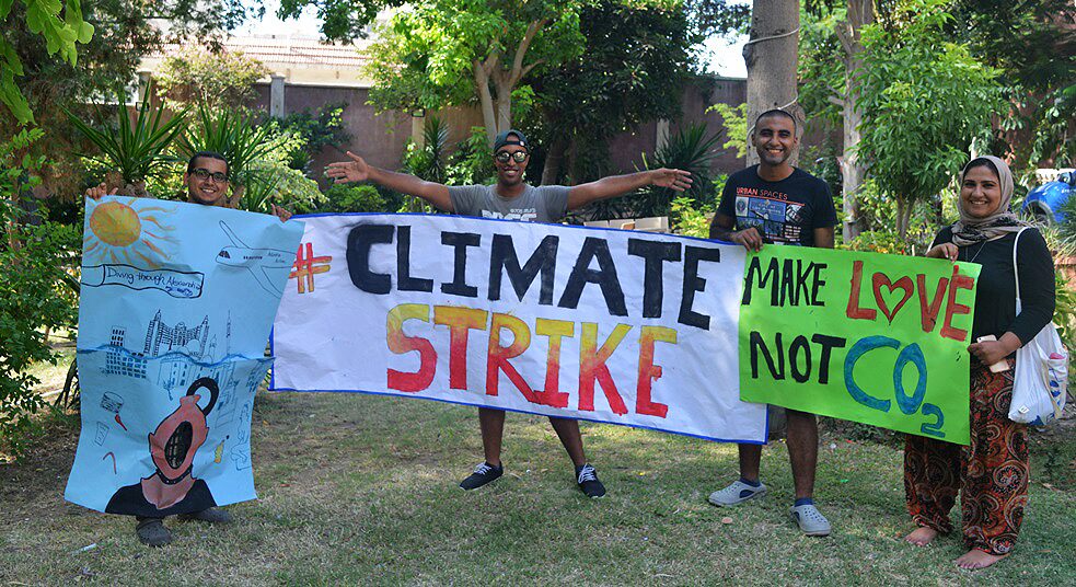 Quatre personnes debout dans un jardin, brandissant des affiches environnementales avec les slogans "Grève pour le climat" et "Faites l'amour, pas le CO2".