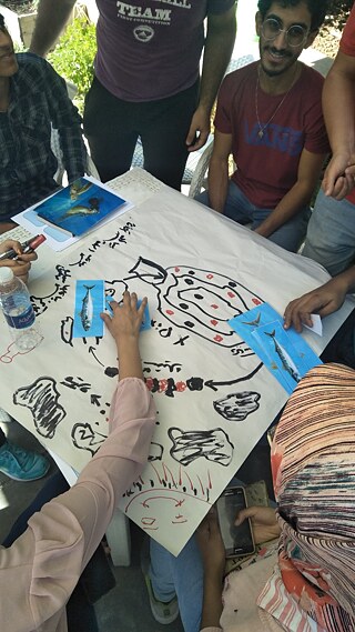 A group of people sitting around a table, looking at a drawing of the sea food chain.