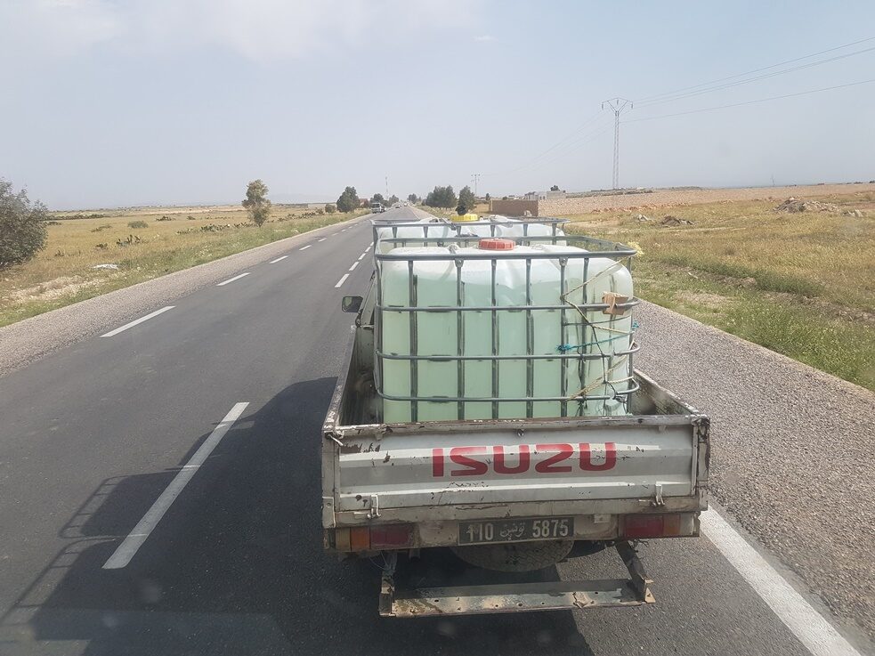A truck driving on the street, with a big container of water in the back.