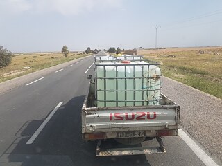 Un camion roulant dans la rue, avec un gros bidon d'eau à l'arrière.