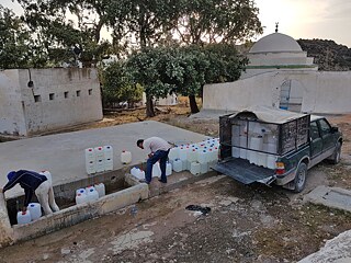 Deux hommes déchargent de gros bidons d'eau d'un camion et les installent.