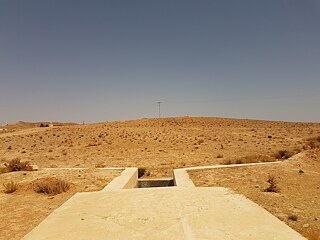 Paysage sec, avec une structure en béton au premier plan visant à récupérer l'eau de pluie.