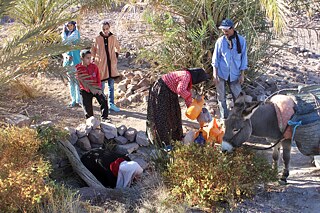 Frauen, Kinder und Männer füllen ihre Wasserkanister an einem Brunnen inmitten einer öden Landschaft auf.