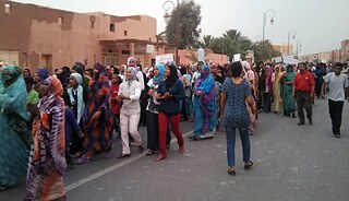 Close-up of a group of people holding a sign with images of people and arabic writing, protesting for their right to water.