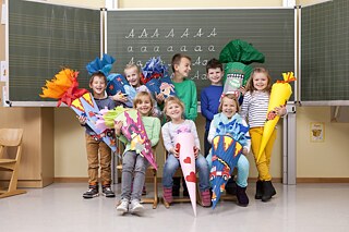 Mehrere Erstklässler stehen am ersten Schultag mit ihren Zuckertüten im Arm vor der Tafel im Klassenraum. Sie lachen und sind fröhlich. © Goethe-Institut e.V. Vorintegration Deutschland – Erstklässler mit Zuckertüten