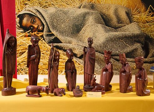 Neue Formen des Dialogs: Weihnachtskrippe aus Ruanda (Leichtholz, rotgewachst), im Hintergrund Flüchtlingskind auf einem Strohbett im Stall, Museum Forum der Völker, Völkerkundemuseum der Franziskaner, Werl