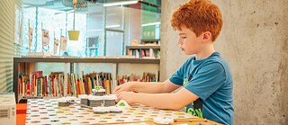 Foto eines Jungs, der in der Bibliothek sitzt und ein Brettspiel spielt
