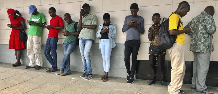Zimbabwe, Mutare, à environ 270 kilomètres à l'est de la capitale Harare, le 23 novembre 2019 : des gens se trouvent dans l'un des rares lieux publics dotés de WIFI gratuit. Selon un récent rapport indépendant, le Zimbabwe dispose de l'une des sources de données les plus onéreuses au monde. Ces coûts de transmission de données élevés s'expliquent essentiellement par le fait que le pays dispose d'assez peu de fournisseurs d'accès mobile à Internet et qu'il s'agit d'un pays enclavé.