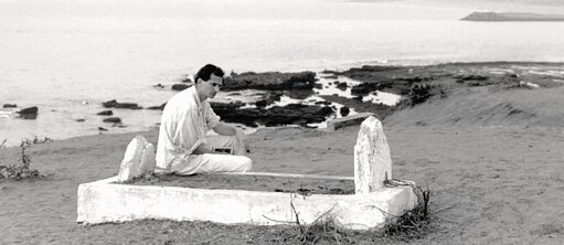 Josef Winkler sur la tombe de Jean Genet sur une plage; la mer en arrière-plan