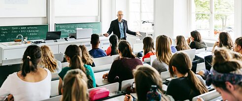 Ein Universitätsprofessor hält einen Vortrag in einem hellen Hörsaal. Bildserie für die Bewerbung der Sprachkurse und Prüfungen in der Region OEZA.