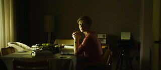 Sandra Hüller sitting at a table in a dark room.