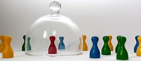 Image of colourful game pieces. One is shielded alone under a glass bell.