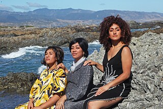 Three women sit on a rocky beach