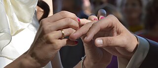 Ein Bräutigam steckt seiner Braut den Ehering an den Finger.