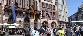 Vor einem Rathaus sind viele Menschen zu sehen. Eine EU-Flagge und eine Deutschlandflagge sind am Rathaus befestigt.