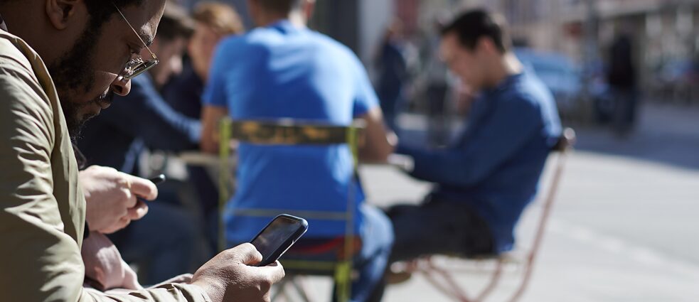 Ein Mann sitzt vor einem Café und nutzt sein Smartphone.