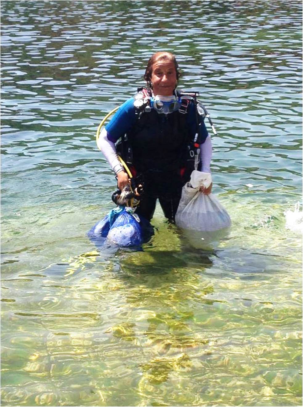 Woman standing in the water, holding up plastic bags.