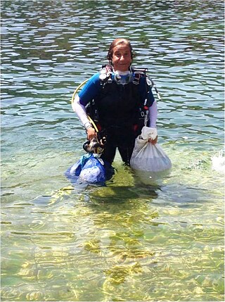 Woman standing in the water, holding up plastic bags.