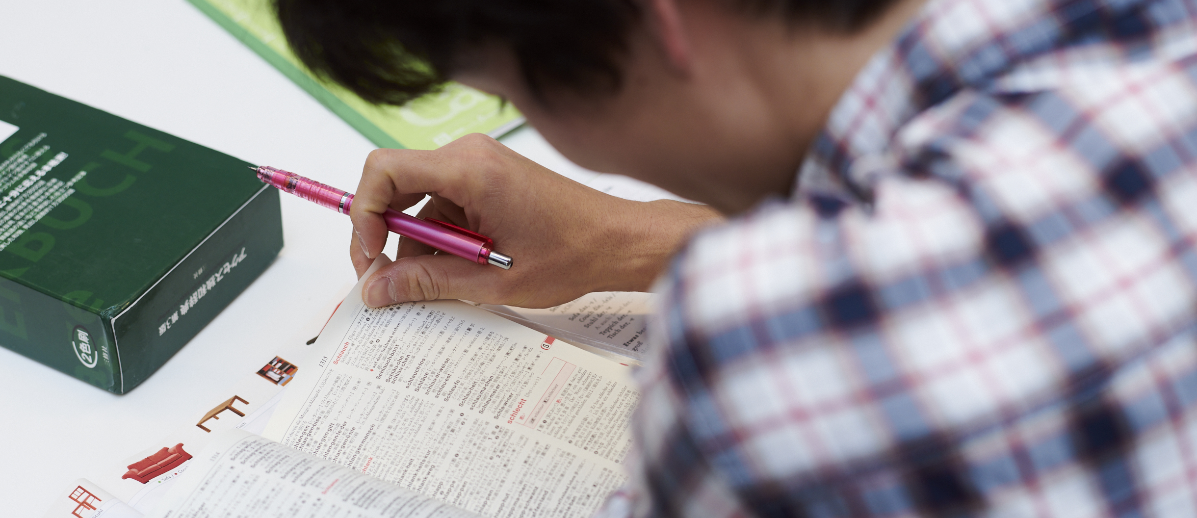 Ein junger Mann hat einen Stift in der Hand und blättert in einem deutsch-chinesischen Wörterbuch.