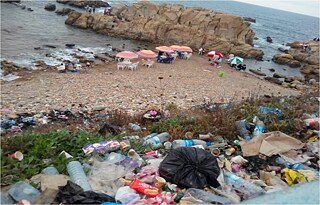 صورة لمنظر مطل على الشاطىء، الكثبان تتكدس فيها أكياس بلاستيكية مملوءة بالنفايات.