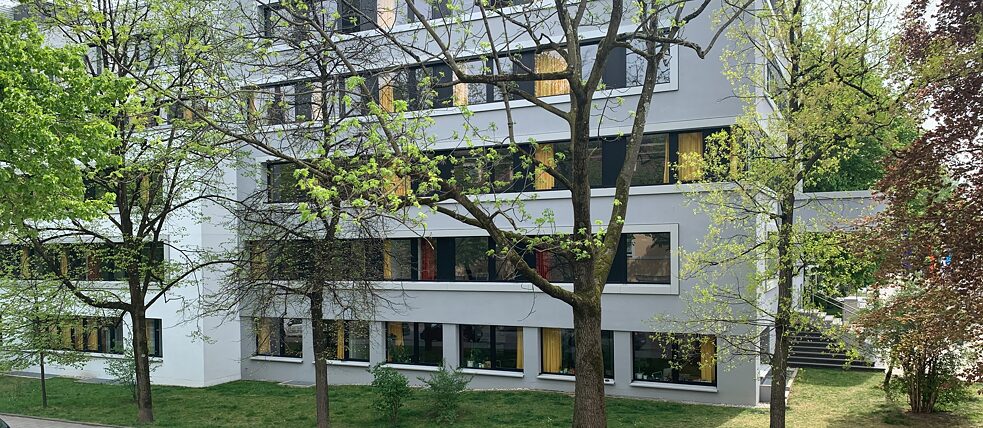 Der Blick aus dem Fenster fällt auf ein graues Gebäude: das Arbeitsgericht. Man kann direkt in den Verhandlungssaal blicken und die Menschen in ihren Gerichtsverhandlungen beobachten. Vorher stehen sie oft nervös in unserer Seitenstraße.