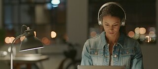 Eine junge Frau mit Kopfhörern lernt Deutsch am Laptop. 