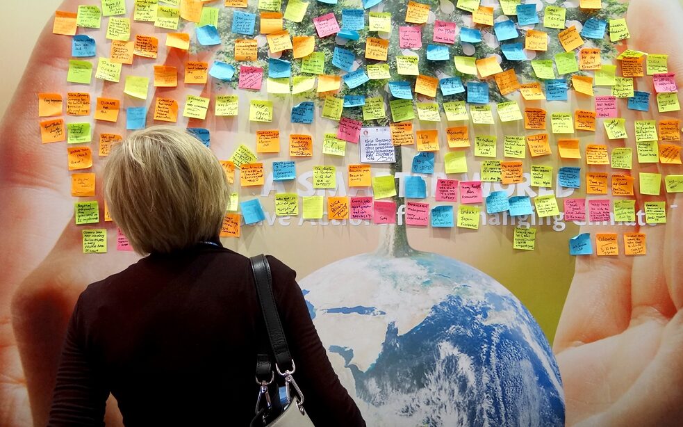 Frau steht vor einer Wand mit vielen bunten Post-it Stickern.