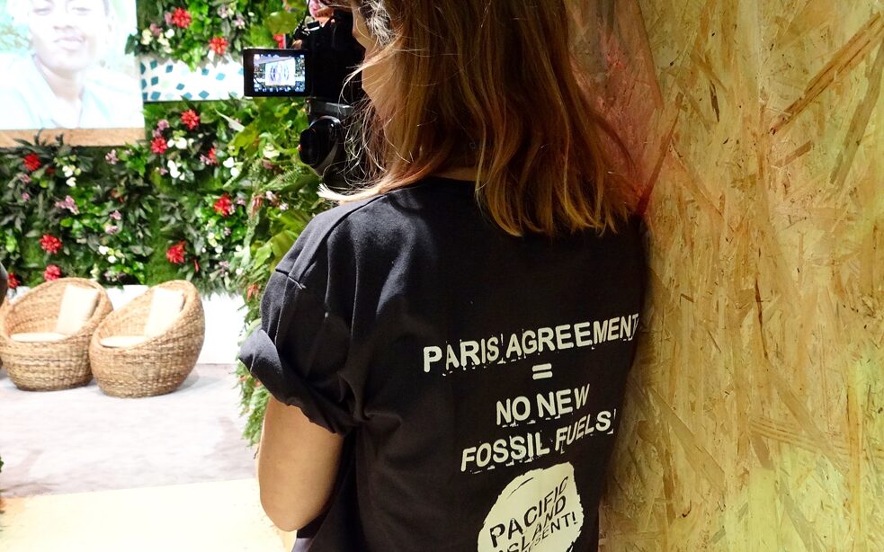 Frau lehnt an Wand und filmt einen Vortrag