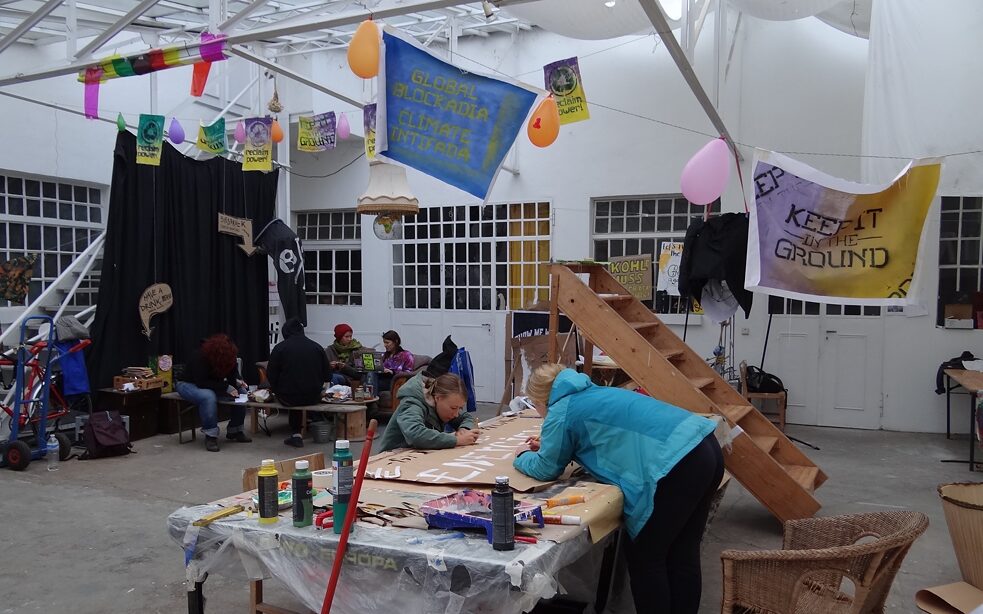 Junge Menschen gestalten Plakat an großem Tisch.