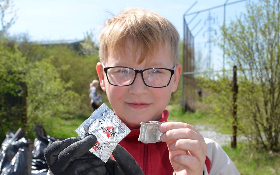Blonder Junge hält Kondom Verpackungen in die Kamera.