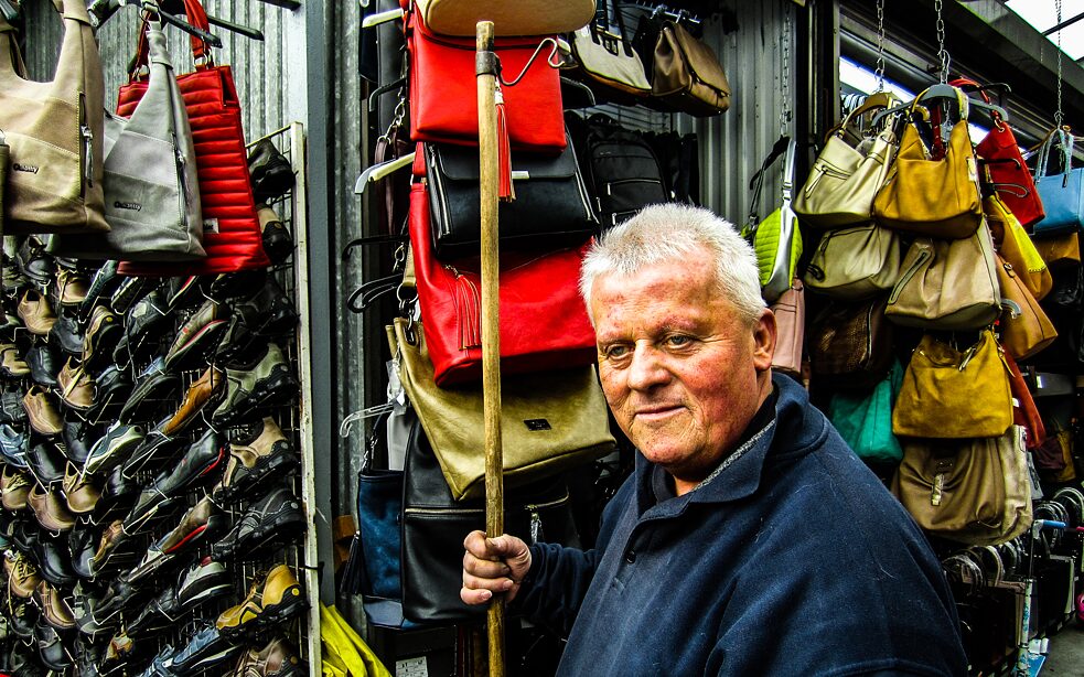Foto von einem Händler vor seinen Taschen und Schuhen.
