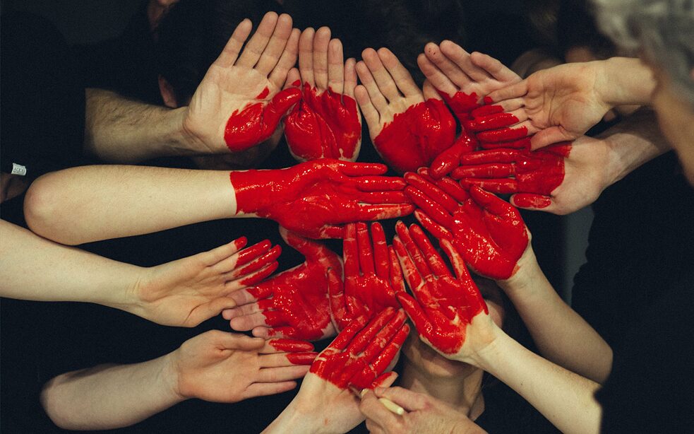 Viele Hände die mit roter Farbe bedeckt sind und ein Herz formen.