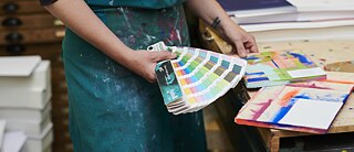 A woman compares a print with a colour chart.