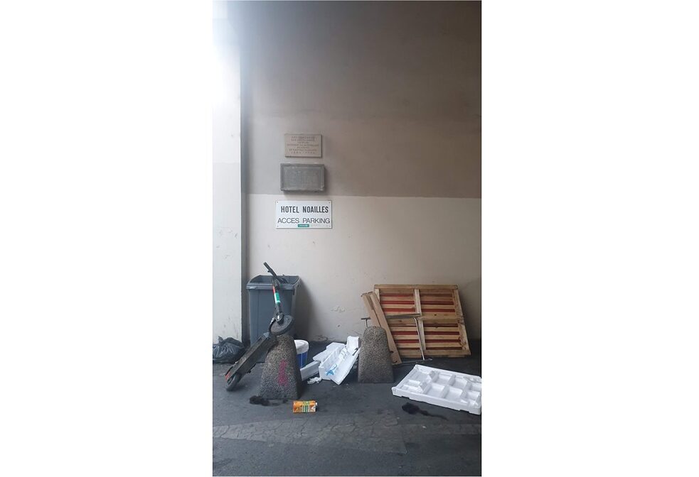 Drei Schilder an Wand über Mülltonne, Roller und Abfall