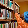 A young Nigerian woman takes a book from a bookshelf in a library. 