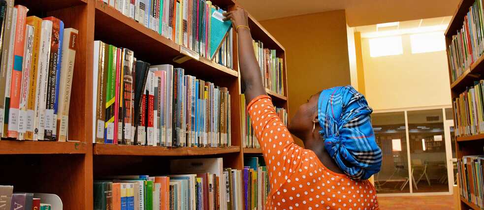 Eine junge Nigerianerin nimmt in einer Bibliothek ein Buch aus einem Bücherregal. 