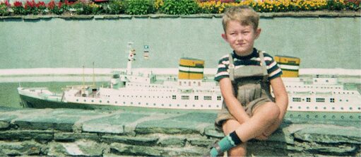 Junge sitzt vor Brunnen mit Modellschiff
