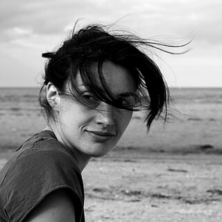 Ein schwarz-weiß Porträt von Nele Brönner am Strand, die Haare wehen ihr ins Gesicht und im Hintergrund sind Wellen zu sehen.