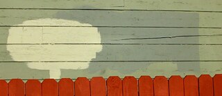 In grün Tönen übermalte Graffiti vor einem rostbraunen Lattenzaun