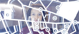 Naine seisab läbipaistva linnaplaaniga puuteekraani taga ja vaatab kaamerasse