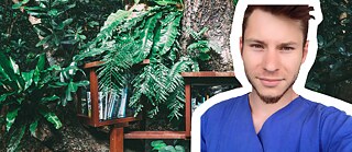 Portrait von Marcel in Ausbildungskluft, vor einem Hintergrund mit Bücherregalen und unechten Bäumen