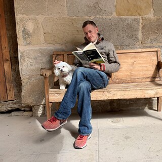 Le rédacteur web Johannes von Stritzky lit « L'Espagne vide » de Sergio del Molino sur un banc à La Fresneda, accompagné de la chienne maltaise Kika.