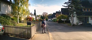Szene aus dem Film „Exil“, ein Mann steht auf einer Strasse mit Einfamilienhäusern