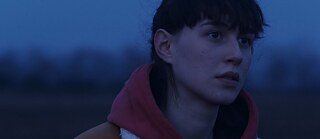 Szene aus dem Film „Nackte Tiere“, Gesicht einer jungen Frau, im Hintergrund ein dunkelblauer Himmel