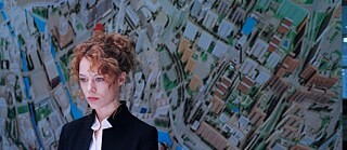 Szene aus dem Film „Undine“, vorne sthet eine Frau, als Hintergrund eine Wand mit dem Stadtplan