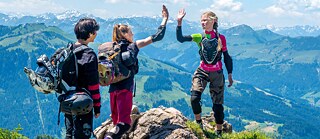 Kaks tüdrukut ja poiss seisavad mäe tipus. Taustal on näha mägesid.